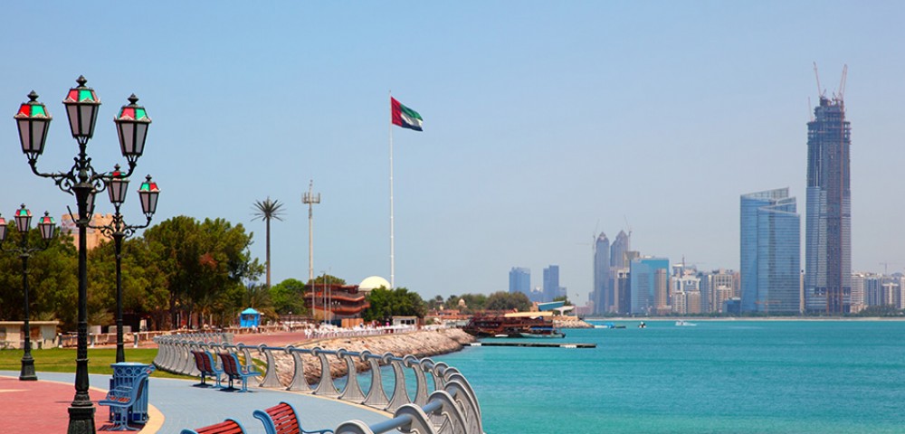 Abu Dhabi high rise buildings on the background of blue sky and Yas Water World on the background of amber sky